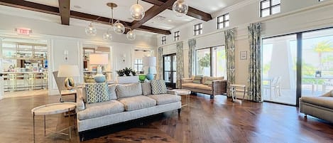 A spacious living room with a large sofa, a coffee table, and a dining area. There is a kitchen visible in the background.