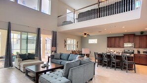 A spacious living area with a high ceiling, a balcony, and a kitchen with dark wooden cabinets.