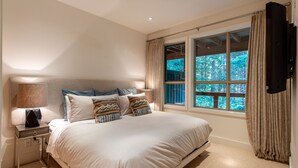 Ein Schlafzimmer mit einem großen Bett, einem Nachttisch, einer Lampe und einem Fenster mit Vorhängen.