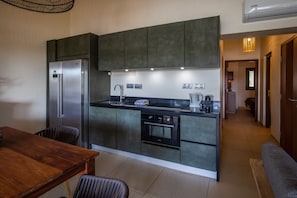 A modern kitchen with a built-in refrigerator, oven, and sink. There is a dining table with chairs and a bench.
