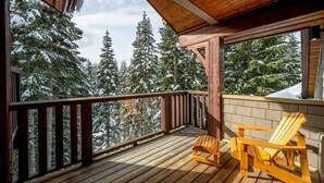 A wooden deck with two wooden Adirondack chairs, a brick wall, and a view of snow-covered trees. - Ski-In/Ski-Out | Modern 4BR | Private Hot Tub | Double Garage | Managed by Aloha Whistler (Whistler)