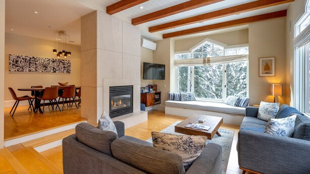 A modern living room with a fireplace, seating area, and large windows offering a view of snow-covered trees. - Ski-In/Ski-Out | Modern 4BR | Private Hot Tub | Double Garage | Managed by Aloha Whistler (Whistler)