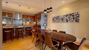 Una cocina moderna con comedor, que incluye una mesa de madera, taburetes de bar e iluminación colgante.