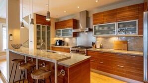 A modern kitchen with a central island, stainless steel appliances, wooden cabinets, and bar stools. - Ski-In/Ski-Out | Modern 4BR | Private Hot Tub | Double Garage | Managed by Aloha Whistler (Whistler)