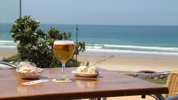 A table with a glass of beer, a basket of bread, and a plate of cookies on a wooden table overlooking a beach. - One bedroom apartment with WiFi (CONIL DE LA FRONTERA)