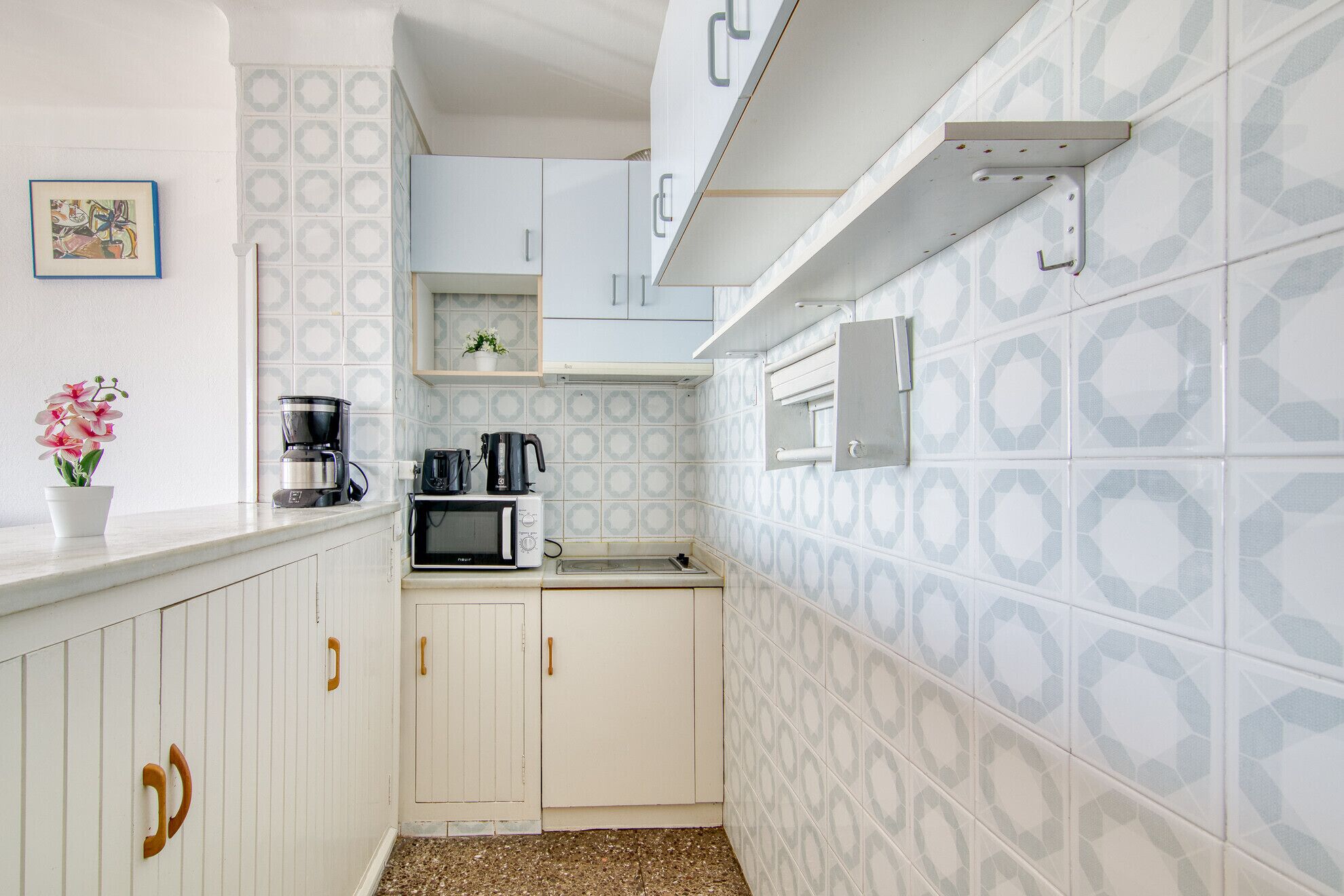 A compact kitchen with white cabinets, a microwave, a coffee maker, and a small potted plant.