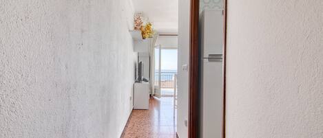 A hallway with a white textured wall, a tiled floor, and a door leading to a balcony with a view.