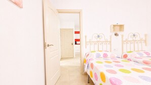 A bedroom with two beds, a door, a hallway, and a red and white striped wall.