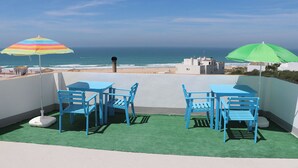 Una terraza en la azotea con una mesa, sillas y dos sombrillas, con vista al océano.
