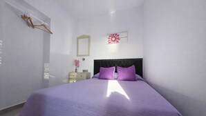 Un dormitorio con cama, mesita de noche, espejo y un adorno en la pared.