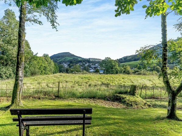 A park with a bench, trees, and a view of a village and hills in the distance.