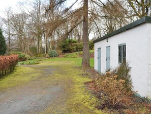 Een wit gebouw met blauwe luiken, omringd door een tuin met een grindpad dat er naartoe leidt.