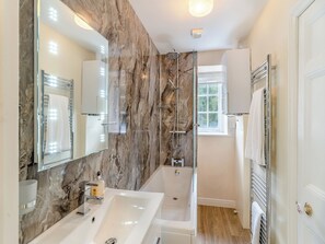 Un baño moderno con pared de mármol, un espejo grande, una bañera y una ducha.