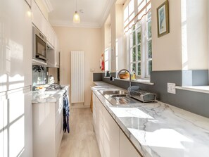 Een moderne keuken met witte kasten, een marmeren aanrechtblad, een inbouwoven en een raam dat natuurlijk licht binnenlaat.