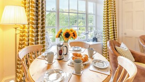 Un coin repas avec une table mise pour le petit-déjeuner, une fenêtre donnant sur un paysage verdoyant et des rideaux à motifs.