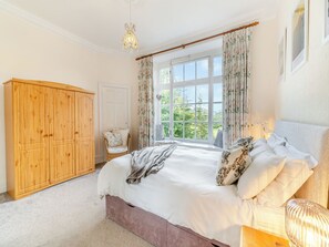 A bedroom with a large bed, a wooden wardrobe, a window with curtains, and a chandelier. - Enjoy stunning fell views from this grand apartment. (Ambleside)