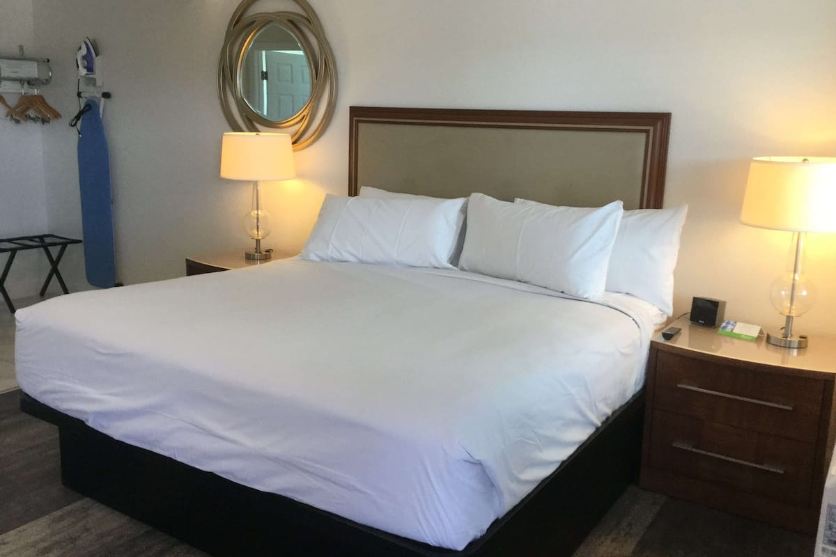 Un lit bien fait, avec du linge de lit blanc, une tête de lit en bois, deux tables de chevet avec des lampes et un miroir au mur.
