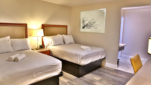 A hotel room with two beds, a desk, a chair, a lamp, and a painting on the wall. - Travelodge by Wyndham Crescent City (Crescent City)