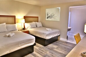 Habitación de hotel con dos camas, un escritorio, una silla, una lámpara y un cuadro en la pared.