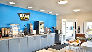 A modern kitchen with a blue accent wall, a coffee station, and a seating area with a table and chairs. - Travelodge by Wyndham Crescent City (Crescent City)