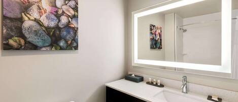 Un baño moderno con un lavamanos blanco, un espejo grande y un inodoro. Hay un perchero con toallas y un pequeño cuadro en la pared.