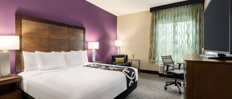 A hotel room with a large bed, two bedside lamps, a desk with a chair, and a television.