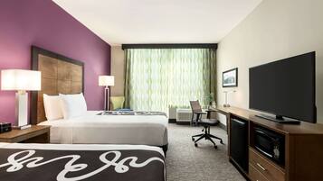 A hotel room with two beds, a desk, a television, and a window with curtains.