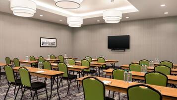A conference room with multiple tables, chairs, and a flat-screen TV on the wall.