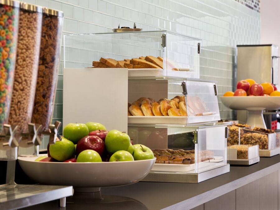 Un bufé de desayuno con diversos alimentos, incluyendo manzanas, bollería y cereales.