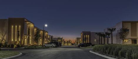 Un quartier résidentiel moderne avec des immeubles bien éclairés, une route dégagée et des voitures garées.
