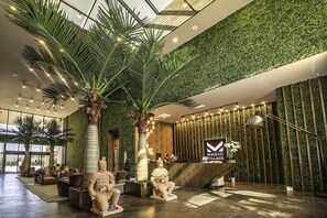 Un área de recepción moderna con una pared verde, palmeras y una estatua de una figura sentada.
