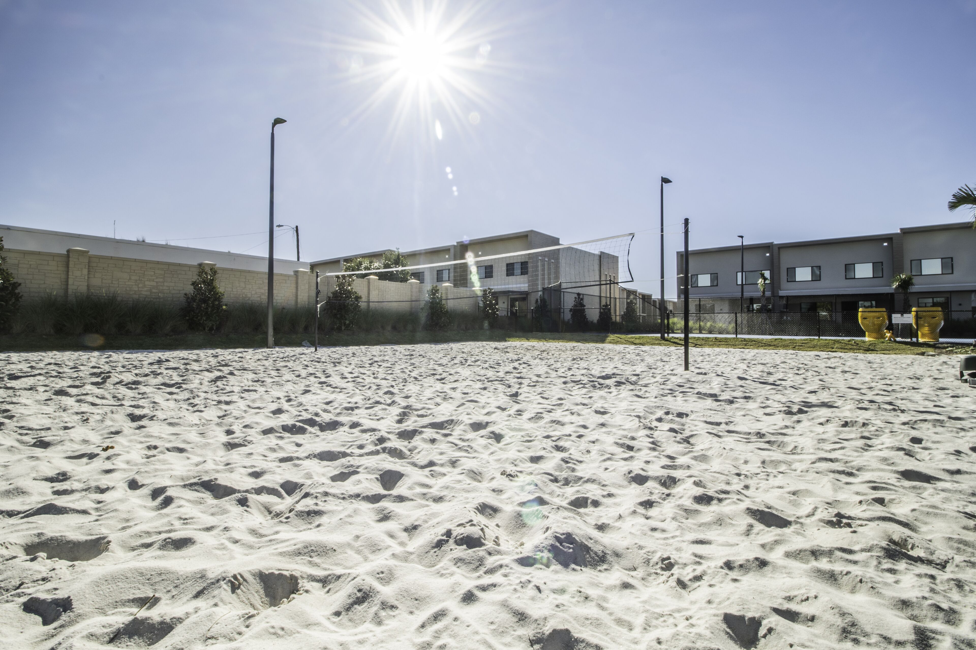 A sandy beach volleyball court with a net, surrounded by buildings and street lamps.