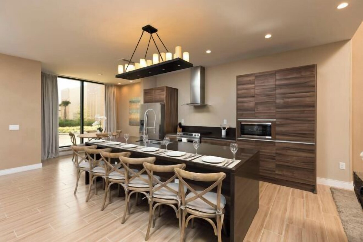 A modern kitchen with a central island, dining chairs, and a large window.