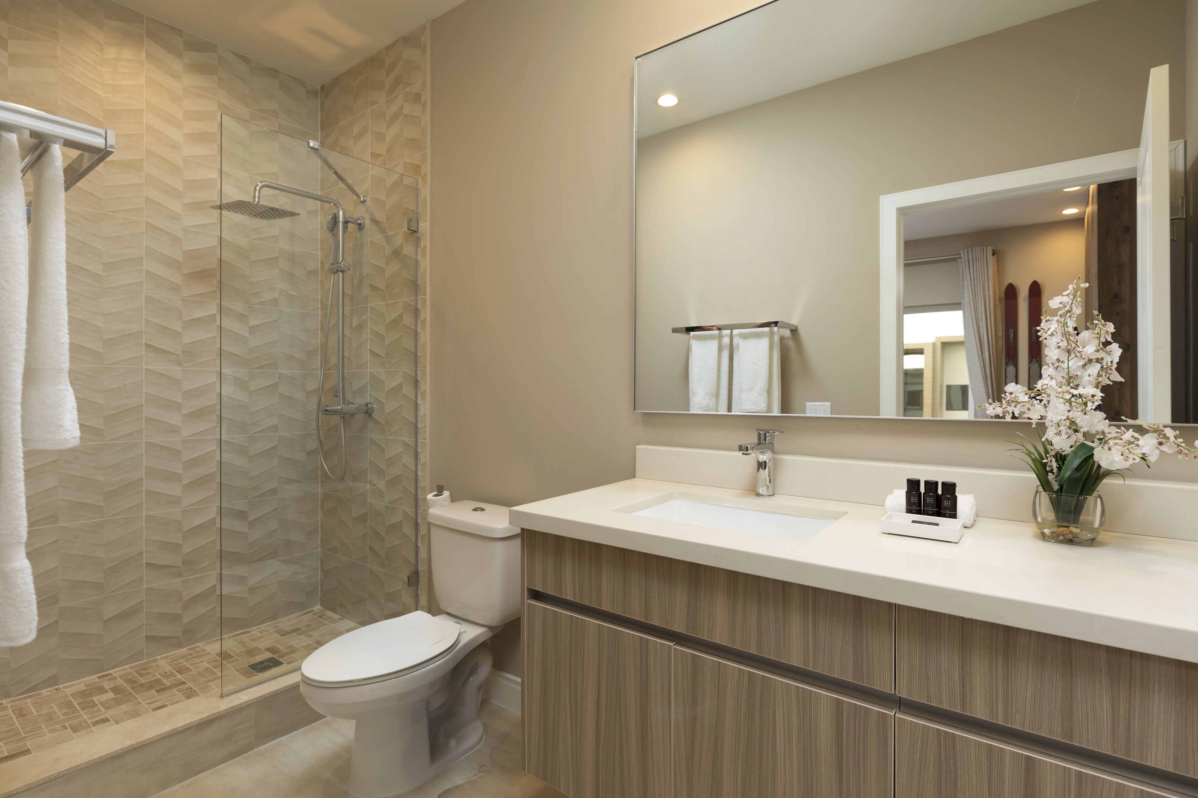 A modern bathroom with a glass-enclosed shower, a white toilet, a vanity with a mirror, and a vase with flowers.