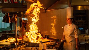Ein Koch in einer professionellen Küche mit großer Flamme, Kochgeräten und einer Edelstahl-Arbeitsfläche.