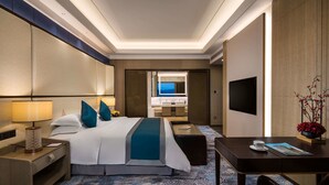 Ein Hotelzimmer mit einem großen Bett, Nachttisch, Lampe, Fernseher und einem Schreibtisch mit Stuhl.