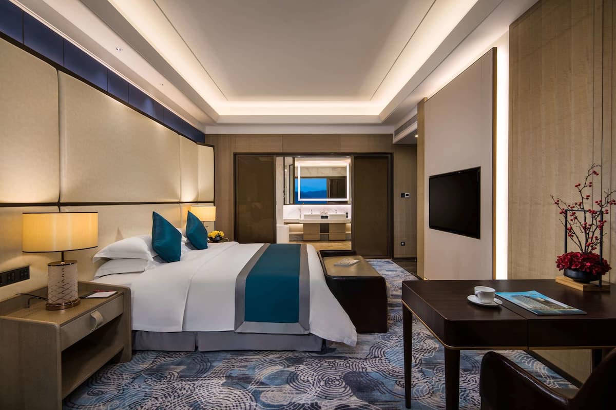 Een hotelkamer met een groot bed, nachtkastje, lamp, televisie en bureau met stoel.
