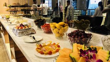 A buffet with various fruits and vegetables, including melon and grapes, on a marble countertop.
