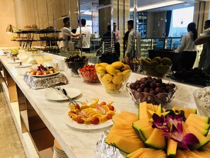Un buffet proposant une variété de fruits et de légumes, notamment des melons et des raisins, sur un comptoir en marbre.