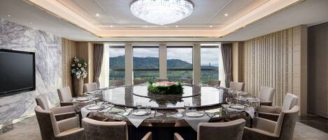 A conference room with a round table, chairs, a chandelier, a flat-screen TV, and a view of the outdoors.