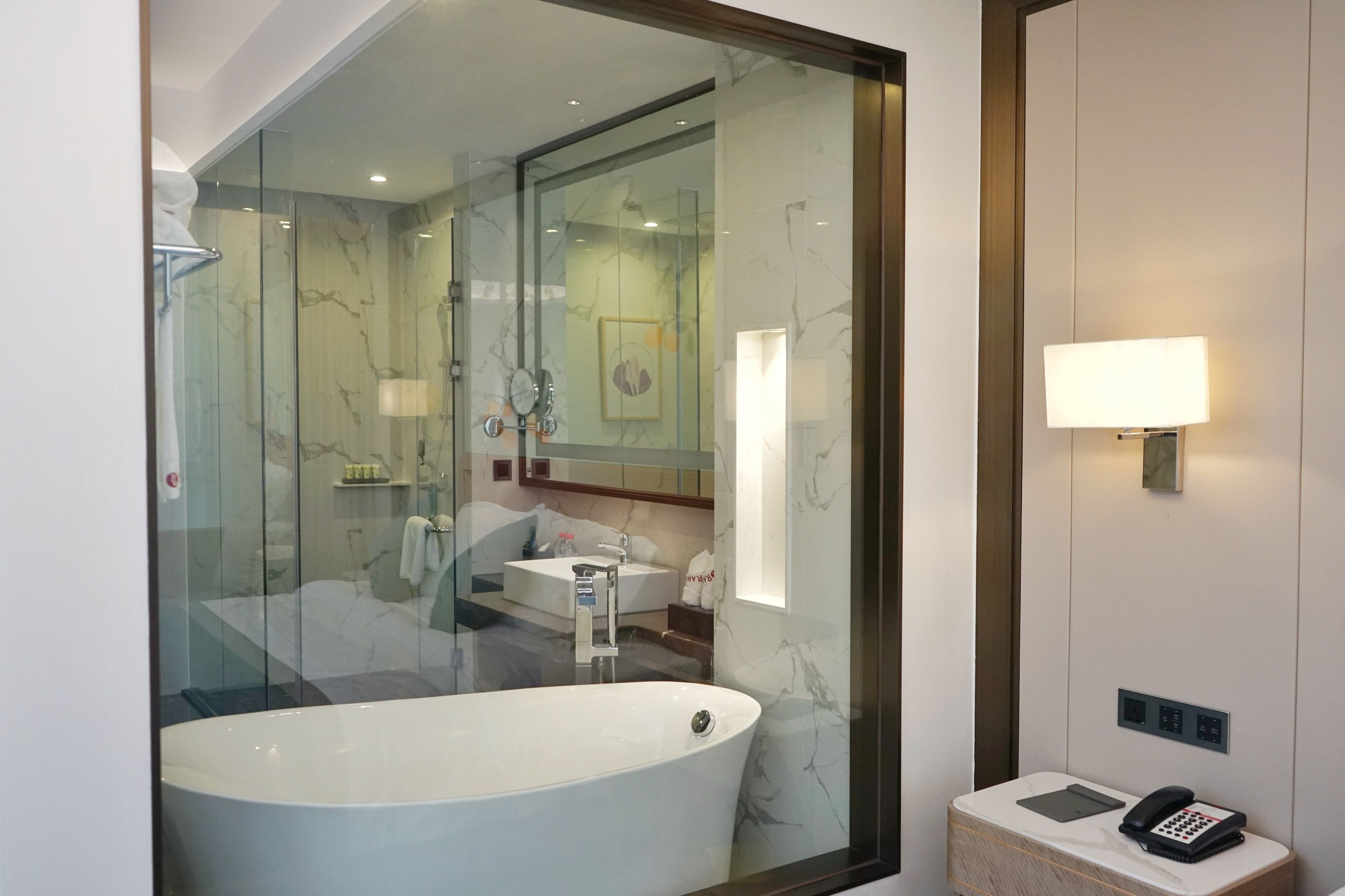 Un baño moderno con una bañera independiente, una ducha con cerramiento de vidrio, un tocador con espejo y un teléfono junto a la cama.