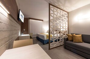 A modern hotel room with a bed, a sofa, a desk, and a TV mounted on the wall. - Microtel Inn & Suites by Wyndham Irapuato (Irapuato)