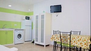 A compact kitchen with a washing machine, a microwave, and a refrigerator. There is a dining table with chairs and a TV mounted on the wall. - Very central apartment with WiFi (CONIL DE LA FRONTERA)