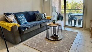 Uma sala de estar com sofá, mesa de centro e porta de vidro deslizante que dá para área externa com mesa e cadeiras.