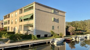 Um edifício de vários andares com varandas, um cais com barcos e um corpo d'água calma que reflete o edifício.
