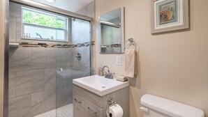 Un baño con ducha de vidrio, lavabo con espejo e inodoro.