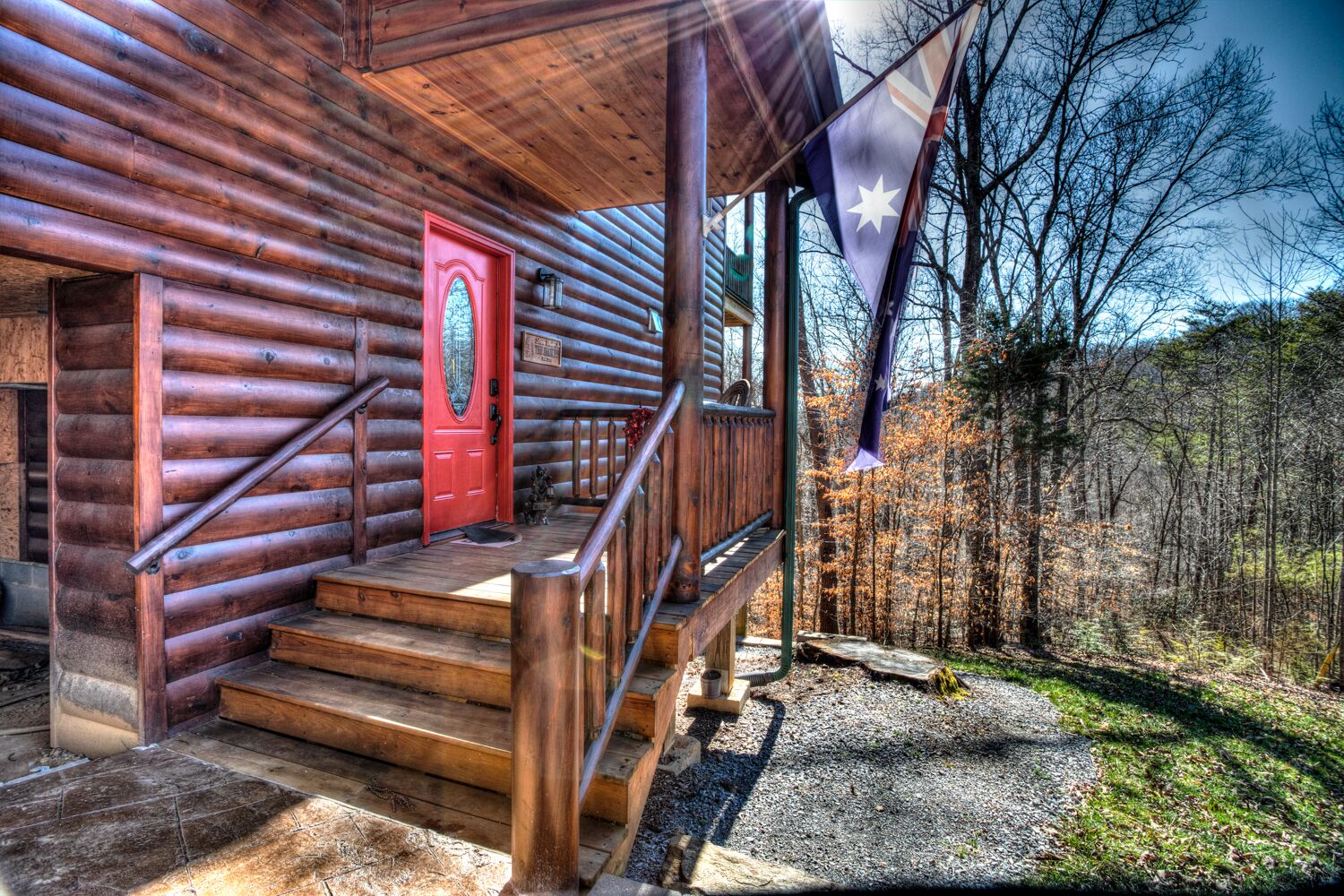 Een vakantiehuisje van hout met een rode deur, houten trappen en een veranda.