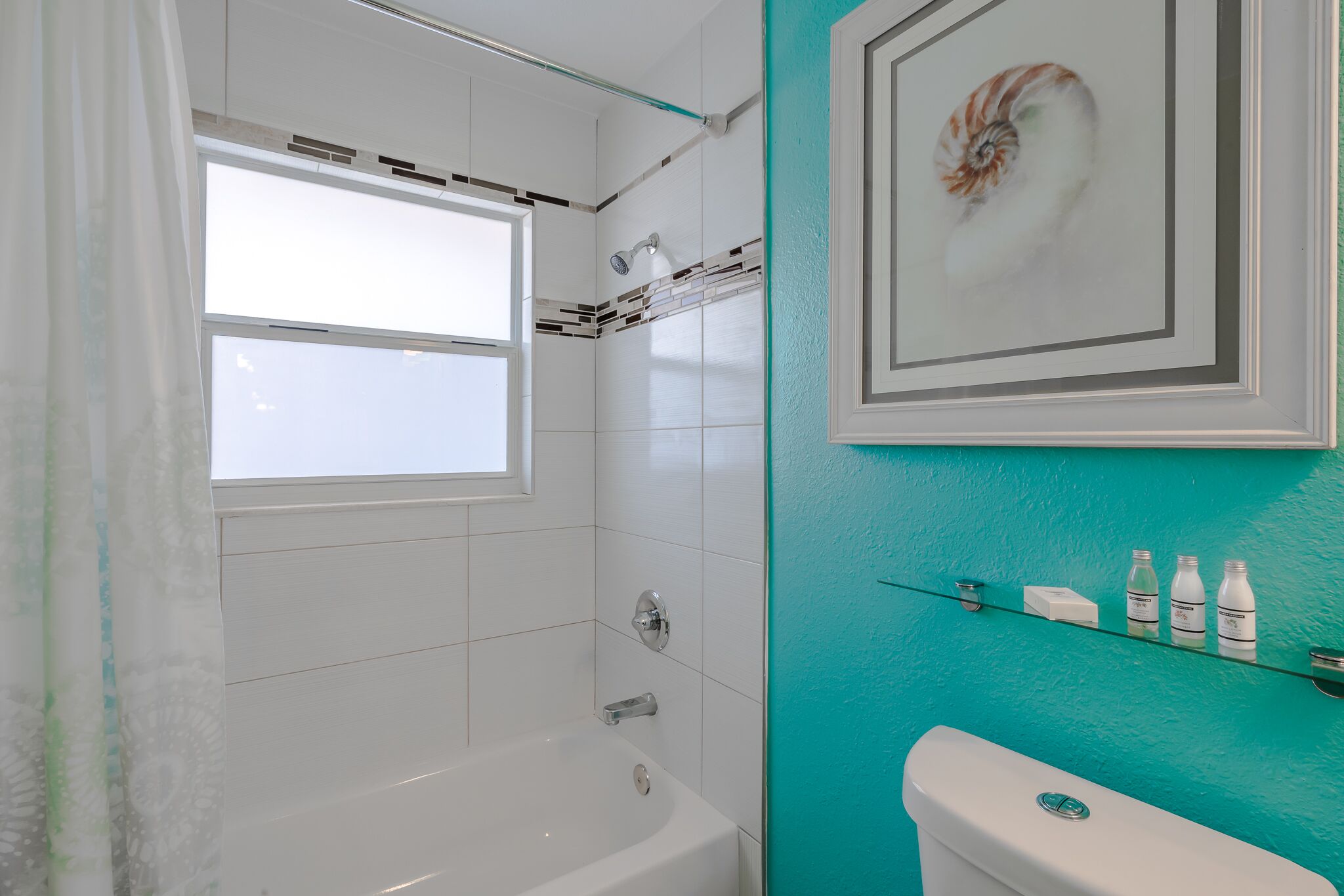 Un baño con bañera, ducha e inodoro. Hay una ventana y un cuadro en la pared.