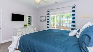 A bedroom with a large bed, a ceiling fan, a TV, a dresser, and a window with curtains.