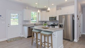 A modern kitchen with white cabinetry, stainless steel appliances, and a central island with bar stools.